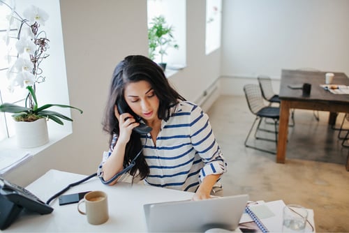 UC Analog vs Digital Article Header Photo of a woman in an office talking on a corded landline while entering notes into her laptop
