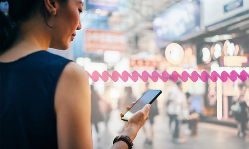 Silent Authentication - content image Woman using smartphone in busy city street, against colorful neon commercial sign and city buildings