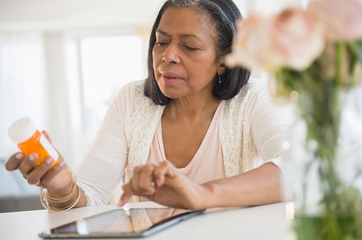 older woman holding prescription bottle and looking at tablet older woman holding prescription bottle and looking at tablet